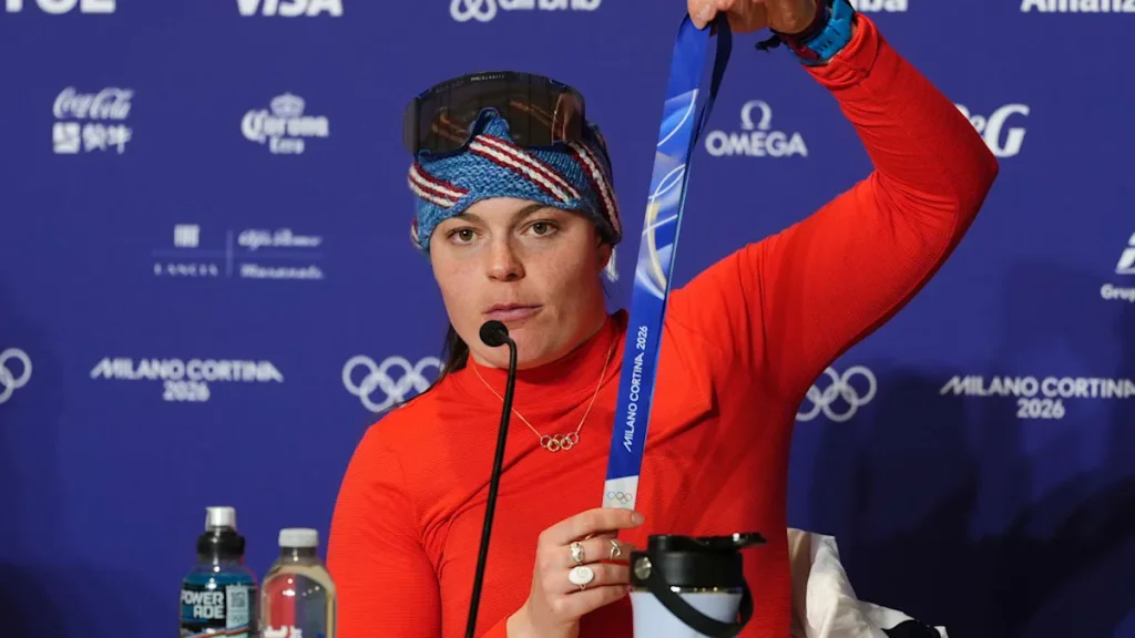 Hlavnou tvárou kuriózneho problému s medailami sa stala americká lyžiarka Breezy Johnsonová. Čerstvá olympijská víťazka v zjazde musela na tlačovej konferencii namiesto športového výkonu vysvetľovať, prečo drží medailu a stuhu oddelene. Zdroj: X/@welt